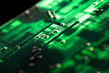 Detail of an illuminated green electronic circuit board with many electrical components, isolated...