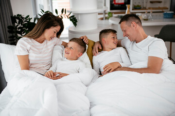 Obraz premium Young family enjoying in bed. Happy parents with sons relaxing in bed