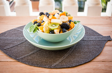Wooden rustic table with a fresh fruit salad in a green plate. Banana, papaya, kiwi, orange, blueberry and berry for an healthy lifestyle