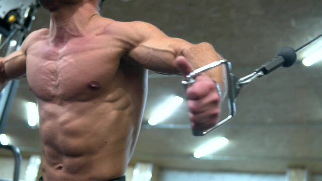 Caucasian male athlete doing bodybuilding cable crossover in a fitness machine. Muscular chest sport exercising close up. Dynamic low angle shot.