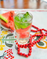 Watermelon smoothie lemonade garnished with watermelon slices and mint leaves served in tall glass on the table outside.