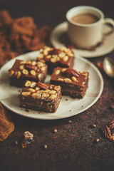 Chocolate cake with caramel frosting, pecans and hot coffee, on rustic background. Freshly baked