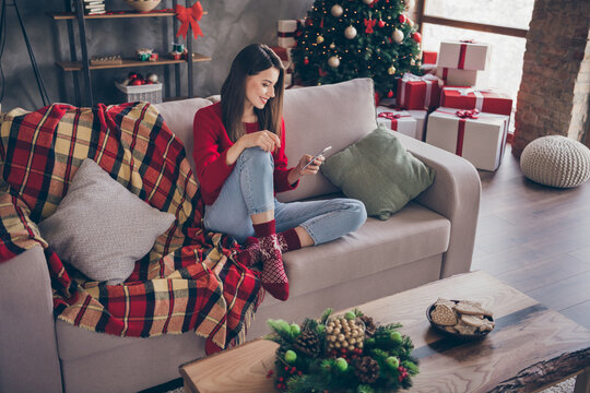 Full body photo of girl sit couch read x-mas news on smartphone in house indoors with christmas spirit ornament tinsels