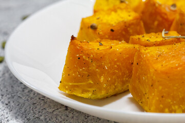 Baked pumpkin in a white plate. Side view. Pumpkin cooked in the oven. Cut pieces of pumpkin.A traditional autumn dish of baked pumpkin.