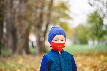 Concept of new normal with little girl in red protective face mask and warm clothes walking in...