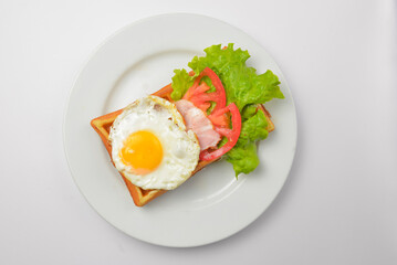 Sour waffle with fried egg and vegetables on a plate. Delicious traditional breakfast idea. Belgian waffle recipe.