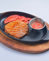 A thick strip steak piece served with tomatoes and sauce in a pan. Delicious bbg meat, barbecue concept.