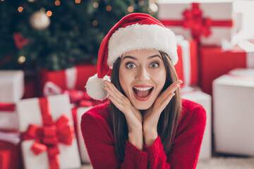 Photo of excited cute lady boxes arms face open mouth wear santa headwear red pullover in decorated x-mas living room indoors