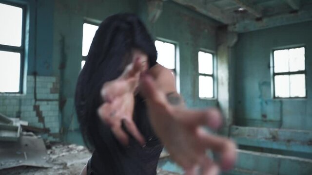 Zombie woman with blood on her face pulls her hands towards the camera in an abandoned building