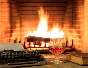 Glass of brandy and a typewriter, logs burning in a fireplace