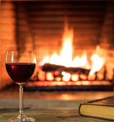 Glass of wine and a book, logs burning in a fireplace