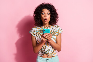 Photo portrait of shocked girl holding cyan smartphone isolated on pastel pink colored background