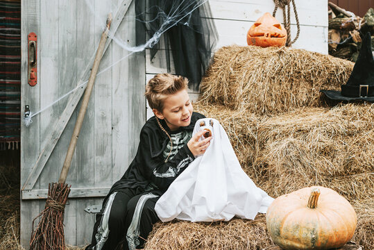 a boy in a skeleton costume with a dog in a ghost costume on the porch of a house decorated to celebrate a Halloween party