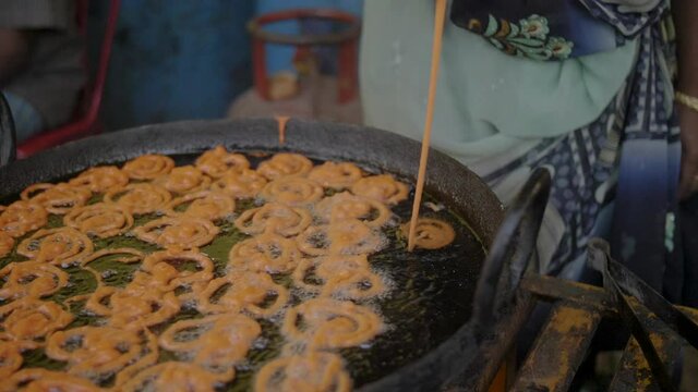 Woman in a dress making traditional orange jalebi snacks on a street food market cinematic 4K