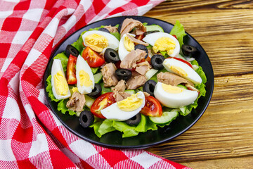 Tasty tuna salad with lettuce, black olives, eggs and fresh vegetables on wooden table
