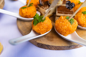 Rounded steamed momordica glutinous rice is placed inside a white spoon and small cakes with different stuffing on party or wedding table.