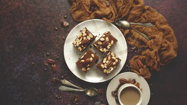 The square pieces of delicious caramel cake with peanuts and brazil nuts served with milk coffee
