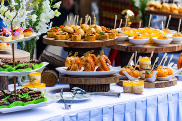 Small cakes, fruit, shrimp skewers and decorations on the white table