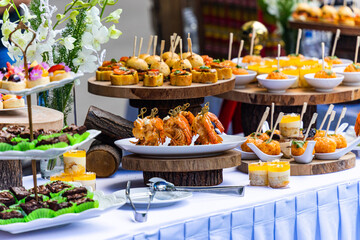 Small cakes, fruit, shrimp skewers and decorations on the white table