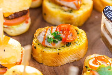 Small burgers, sliced bread and pork bologna on wooden cutting board.