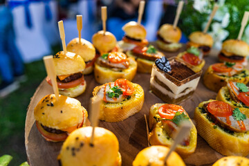 Small burgers, sliced bread and pork bologna on wooden cutting board.