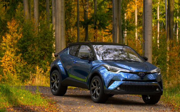 hybrid Toyota C-HR crossover SUV on a road leading through the autumn forest