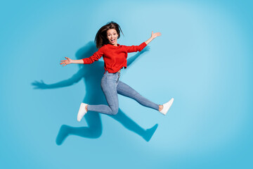 Full length photo of crazy lady jump high up wear knitted red sweater sneakers jeans isolated blue color background