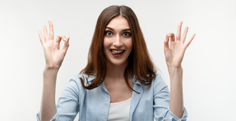 Portrait of a happy young woman with long chestnut hair showing OK gesture. Human emotions, facial expression concept