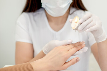 Manicure master applying warm wax from candle on fingernails of young woman in nail salon