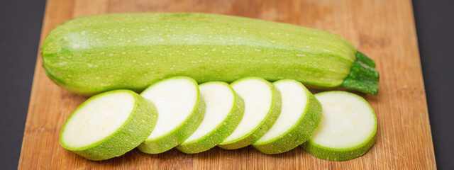 Slices of courgettes on wooden chopping board. Fresh green zucchini whole and cut into slices on cutting board