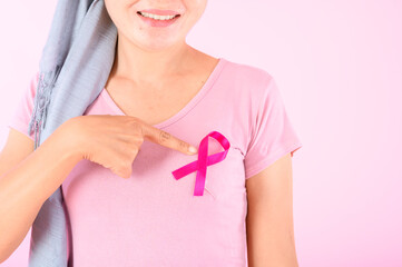 Muslim woman wearing a hijab with a ribbon on her chest shows prevention of breast cancer. On a pink backdrop, breast cancer concept, cancer prevention concept.