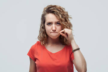 Young woman showing zip gesture as if shutting mouth on key, promises to keep secret. Silence and...