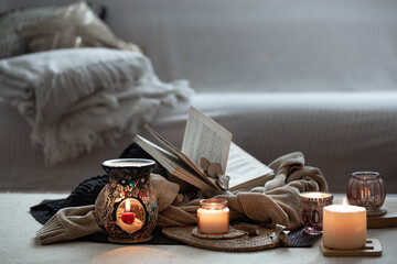 Still life of burning candles, books on sweaters on a blurred gray background. Winter mood, home decoration