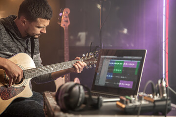 Fototapeta na wymiar Professional musician recording in studio. Guitarist sitting in front laptop monitor in recording studio.