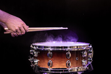 Drum sticks hitting snare drum with splashing water on black background under studio lighting.