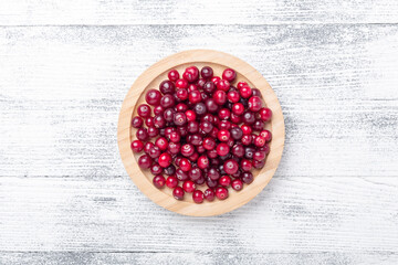 Raw fresh cranberries in wooden bowl on light wood background. Top view