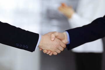 Business people shaking hands at meeting or negotiation, close-up. Group of unknown businessmen and a woman standing in a modern office. Teamwork, partnership and handshake concept