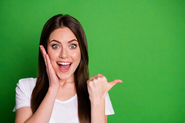 Fototapeta Photo portrait of cheerful girl pointing finger at blank space touching face with one hand isolated on vivid green colored background obraz