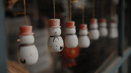 Christmas toys snowmen hang on a thread behind the glass in the house