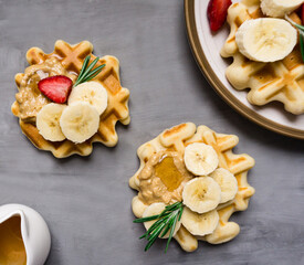 Belgian breakfast waffles with strawberries, peanut butter, banana and syrup lie on a concrete background.
