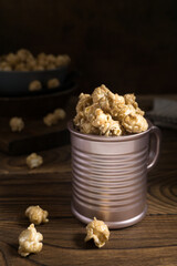 A metal bowl filled with sweet popcorn stands on a dark wooden surface. Popcorn is scattered nearby.