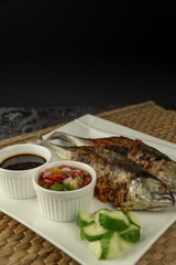 Grilled Torpedo Scad fish (Ikan Cencaru Bakar in Malay) with hot soy sauce, hot tamarind juice and fresh cucumber on white plate