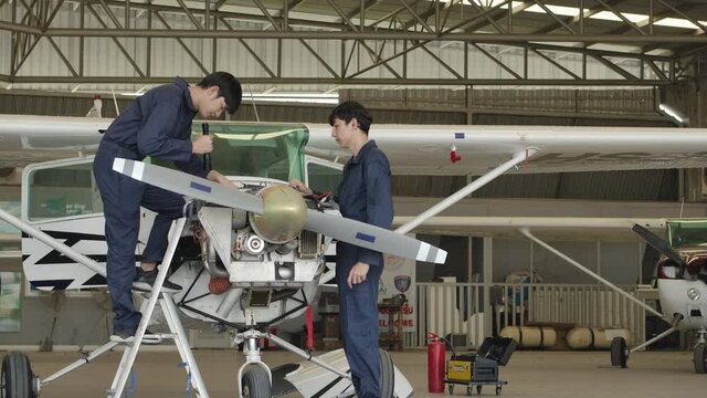 Two young asian aviation maintenance engineer doing a pre flight checkup or maintenance on a small engine aircraft using digital tablet in hangar. Transportation and Technology concept.