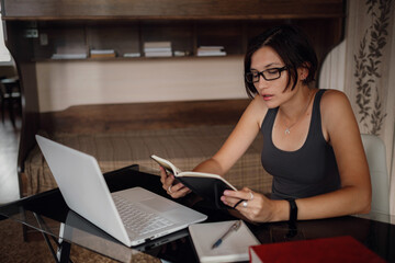 Young female student in glasses using laptop, communicates on internet with teachers.