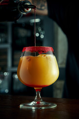 The bartender prepares an alcoholic cocktail. The process of pouring red liquid from a shaker into a beautiful glass with ice at the bar. Bar accessories