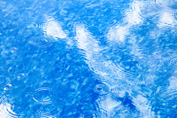 Fototapeta na wymiar Raindrops on pool blue water surface. Blue water texture as background. Stains circles on the water from rain
