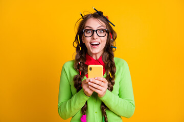 Photo of amazed girl with pencil hairdo hold cellphone wear shirt isolated on yellow color...