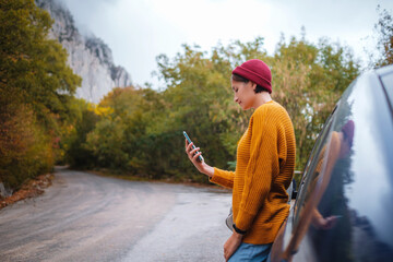 Naklejka premium Woman beside a car and looking at smart phone.