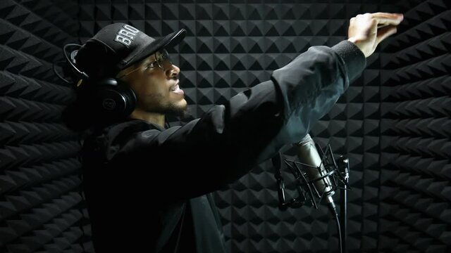 Mixed race male rap singer recording a vocal and singing his song in the microphone in the sound studio room, front view