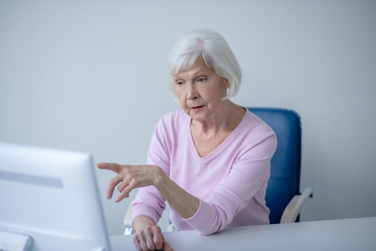 Grey-haired elderly woman sitting in front of computer and showing something